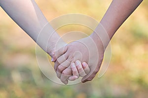 Kids` hands holding for support and friendship, blur green grass