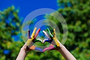 Kids hands painted in bright colors make a heart shape on summer nature background