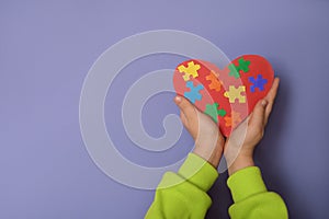 Kids hands with a red heart with pieces of colored puzzles inside