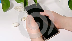 Kids hands with a smartphone on a white background with plants. Digital devices. Social networks, online communication, shopping,