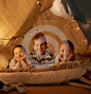 Kids, happy and playing in blanket fort with portrait for fantasy, bonding and fairy lights at night. Friends, children