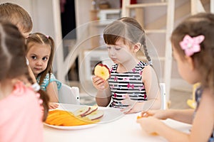 Kids have a lunch in daycare centre. Children eating fresh fruits in kindergarten