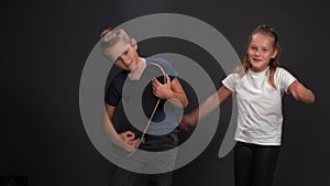 Kids are having fun on black background. Boy plays on the panelboard, as on the hyitar. Girl next to her dances