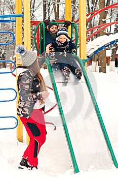 Kids having fun at winter playground. Winter holidays. Mother helps her little son to go down on a slide