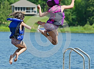 Kids having summer fun jumping off dock into lake