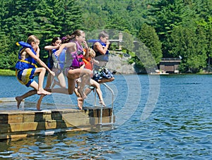 Kids having summer fun jumping off dock into lake photo