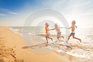 Kids holding hands and running along sandy beach