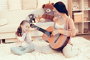 Mom with Guitar in Hand and Girl Sitting on Carpet