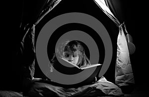 Kids in kids tent reading books. Child reading story with book. Kids face with night light. Concept of education and
