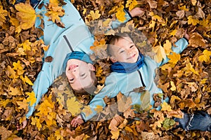 Kids laying on fallen leaves in autumn park
