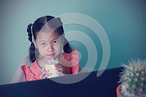 Kids learning education online using computer. Asian girl drinking milk before distance learning online. Due to coronavirus