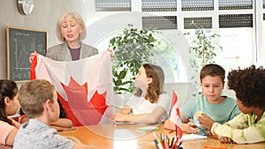 Kids learning together about canada in geography class Female teacher showing canadian flag to kids in geography