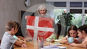 Kids learning together about denmark in geography class Female teacher showing danish flag to kids in geography class