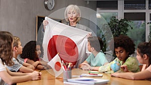 Kids learning together about japan in geography class Female teacher showing japanese flag to kids in geography