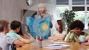 Kids learning together about kazakhstan in geography class Female teacher showing kazakh flag to kids in geography