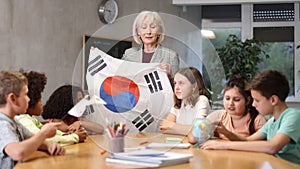 Kids learning together about south korea in geography class Female teacher showing south korean flag to kids in