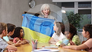 Kids learning together about ukraine in geography class Female teacher showing ukrainian flag to kids in geography