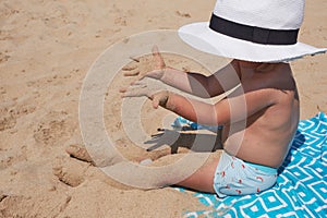 Kids lifestyle outdoor. Happy cute boy in panama playing with sand on the beach of sea. Summer vacation and family