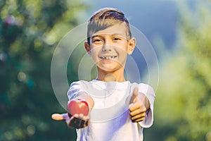 Close up portrait of joyous boy with fresh apple, giving thumb up with satisfaction.