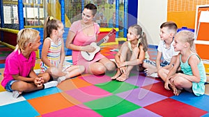 Kids listening smiling teacher playing small guitar