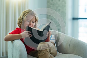 Kids and literature. Child reading book, sitting at home in cozy living room on couch. Concept of education, childhood