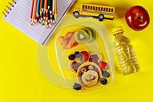 Kids lunch box with pancake, berries, drink and apple on yellow background