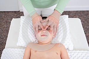 Kids massage concept background. Female therapist giving a young boy face massage. Top view.