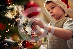 A little boy decorating a Christmas tree with his mother at home. Together, New Year, family, celebration