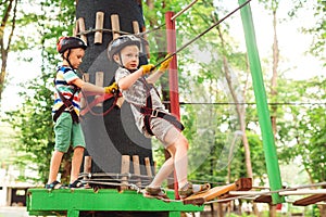 Kids passing the cable route high among trees. Kids in safety helmets, extreme sport in park