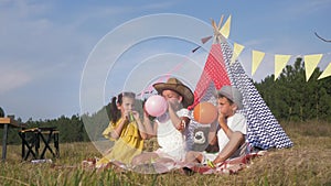 Kids picnic games, funny boy and girls are happy to inflate colorful balls to decorate wigwam on weekend in fresh air