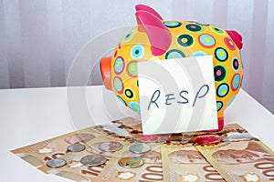 Kids piggy bank with one hundred dollars and RESP sticky note