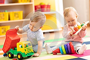 Kids play with educational toys. Children sit on a rug in a play room at home or kindergarten. Toddler boy with toy