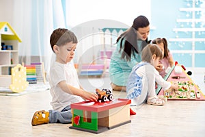 Kids play with educational toys, educator looking after pupils in kindergarten