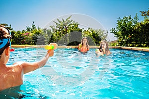 Kids play in swimming pool shooting with water-gun
