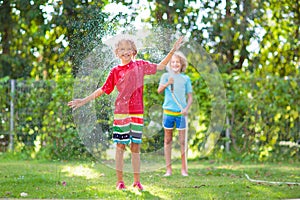 Kids play with water sprinkle hose. Summer garden