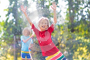 Kids play with water sprinkle hose. Summer garden