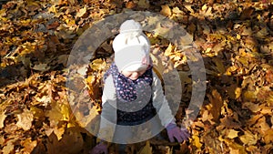 Kids playing in autumn park. A little girl lies in a pile of yellow leaves, leaves pour down on top of her, joy