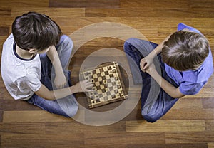 Kids playing chess sitting on wooden floor. Top view. Game, education, lifestyle, leisure concept