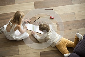 Kids playing drawing together on floor at home, top view