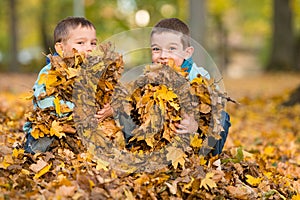 Kids playing with fallen leaves in autumn park