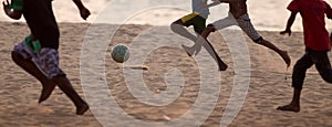 Kids playing football barefoot on sand