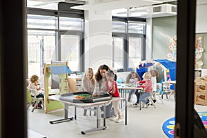 Kids playing games with a female teacher in a classroom in an infant school, seen from doorway photo