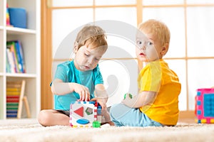 Kids playing with logical toy on soft carpet in nursery roomor kindergarten. Children arranging and sorting shapes or sizes.