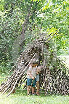 kids playing next to wooden stick house looking like indian hut, tepee