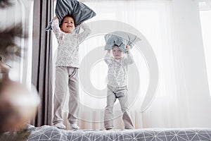 Kids playing in parents bed. Children wake up in sunny white bedroom. Boy and girl play in matching pajamas. Family