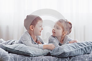 Kids playing in parents bed. Children wake up in sunny white bedroom. Boy and girl play in matching pajamas. Sleepwear