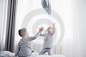 Kids playing in parents bed. Children wake up in sunny white bedroom. Boy and girl play in matching pajamas. Sleepwear