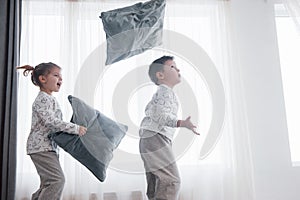 Kids playing in parents bed. Children wake up in sunny white bedroom. Boy and girl play in matching pajamas. Sleepwear