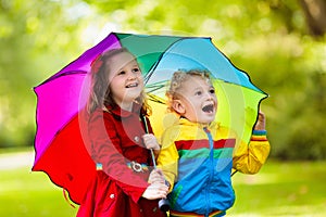 Kids playing in the rain under colorful umbrella