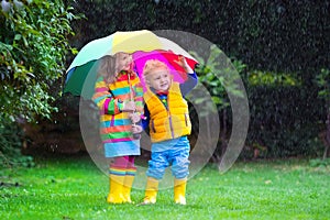 Kids playing in the rain under colorful umbrella